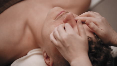physician-is-massaging-acupuncture-point-on-face-of-male-patient-in-clinic-of-alternative-medicine-acupressure-session